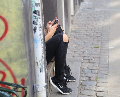 Mädchenbeine am Gehsteig mit Handy